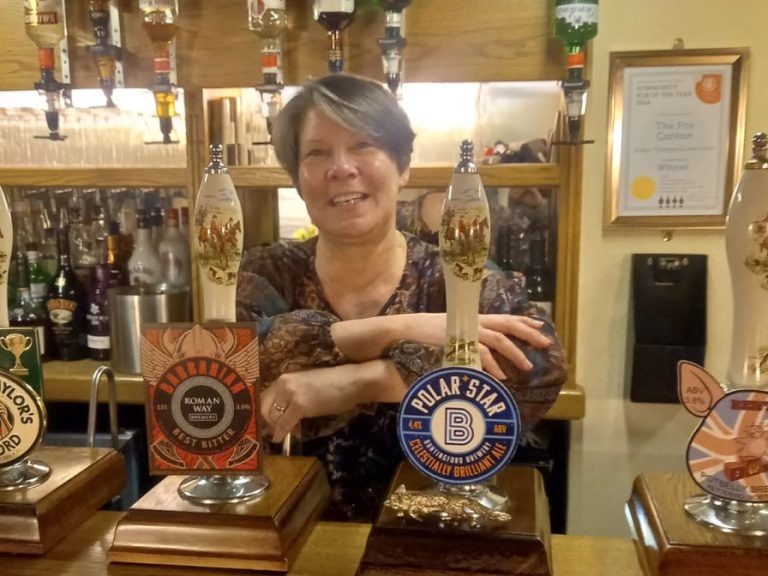 Alison Thompson, landlady of the award-winning The Fox at Carlton. She is standing behind the bar and leaning on the beer pumps.