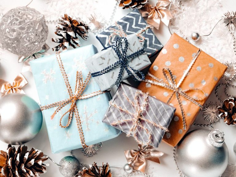 An overhead shot of some beautifully wrapped gifts surrounded by snow-dusted pine cones and Christmas baubles