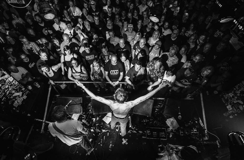 Indie band Deadletter are performing on the main stage at Esquires. The photograph is black and white and taken from immediately above the stage, giving a birds' eye view of the band and the audience. The singer has his arms outstreched.