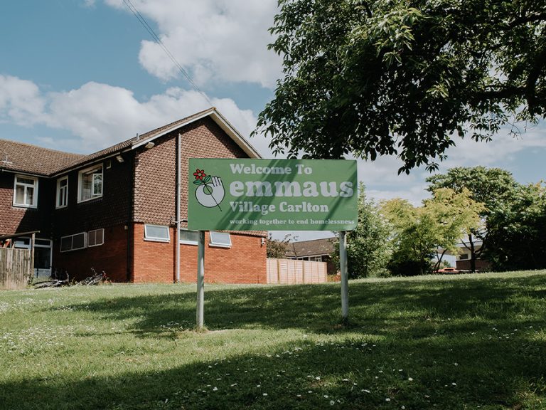 Emmaus Village Carlton sign with the village in the background