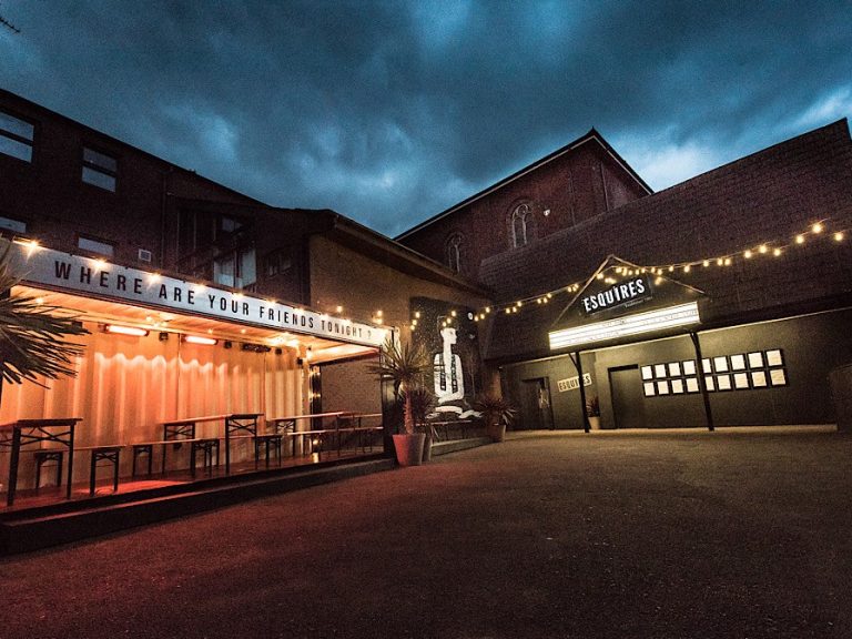 The exterior of Esquires live music venue in Bedord. It has an inviting outdoor seating area and festoon lights.