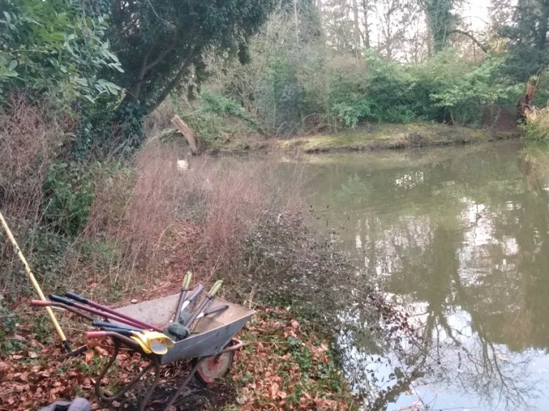A wheelbarrow and gardening tools on the overgrown path around the lake in Bedford Park