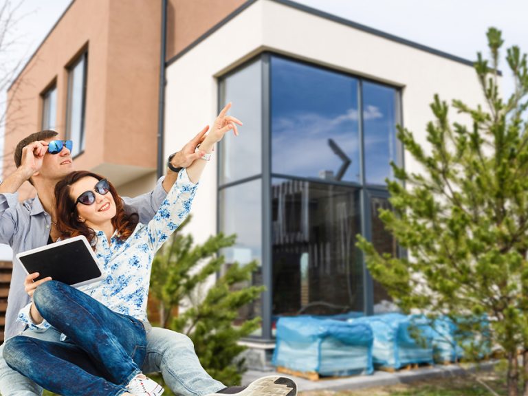 Happy couple with their new house at the background and smiling. Image: Gray StudioPro/FreePik