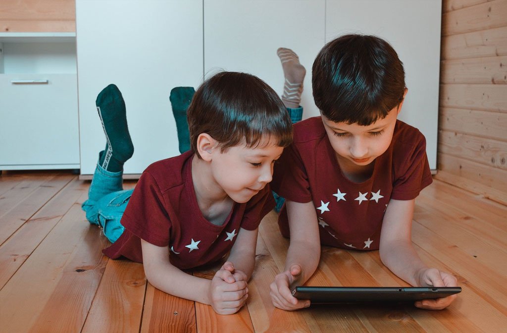 Two young boys laying on their stomachs, propped up on their elbows and watching a tablet. Image:image Pixabay/Vika Glitter