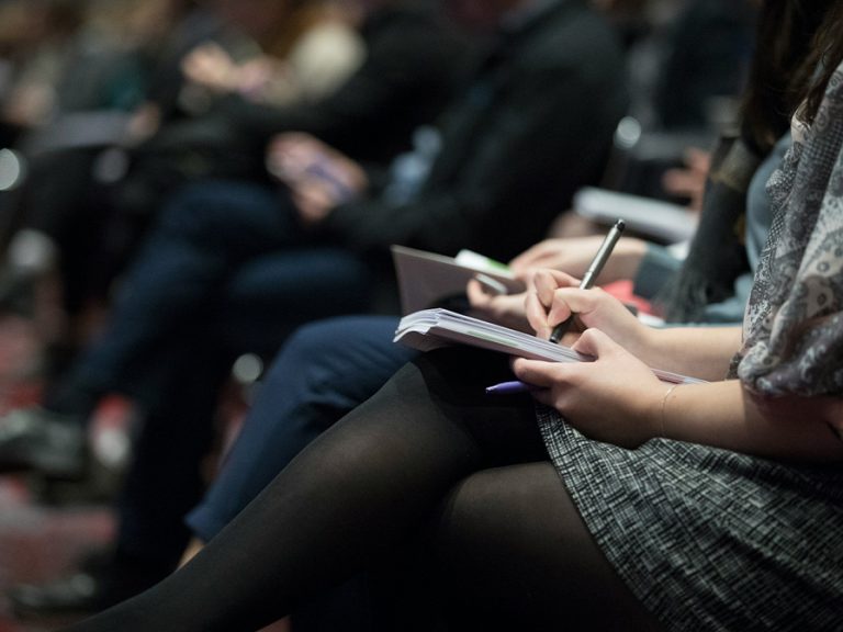 Journalists taking notes at a conference.