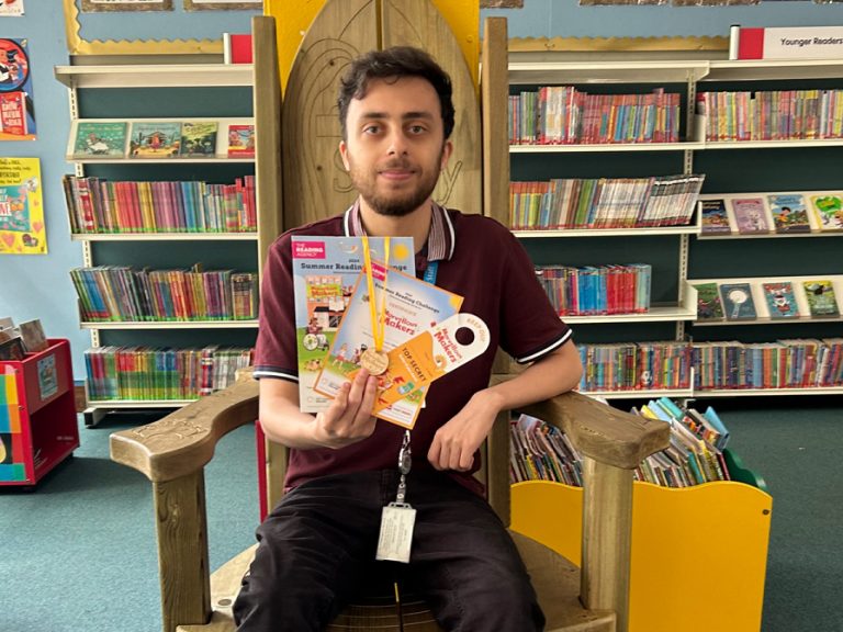 Michael Gordon, a library support officer at Putnoe Library shows off what young readers could win in the Summer Reading Challenge 2024. Image: Bedford Borough Council.