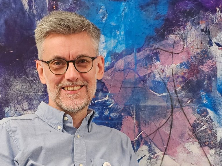 PK (Paul Kellett) standing in front of one of his abstract paintings