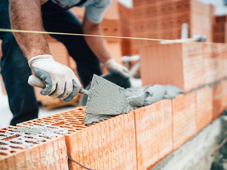 Professional worker using pan knife for building brick walls with cement and mortar planning new homes builder building Image Adobe Stock:aboutmomentsimages