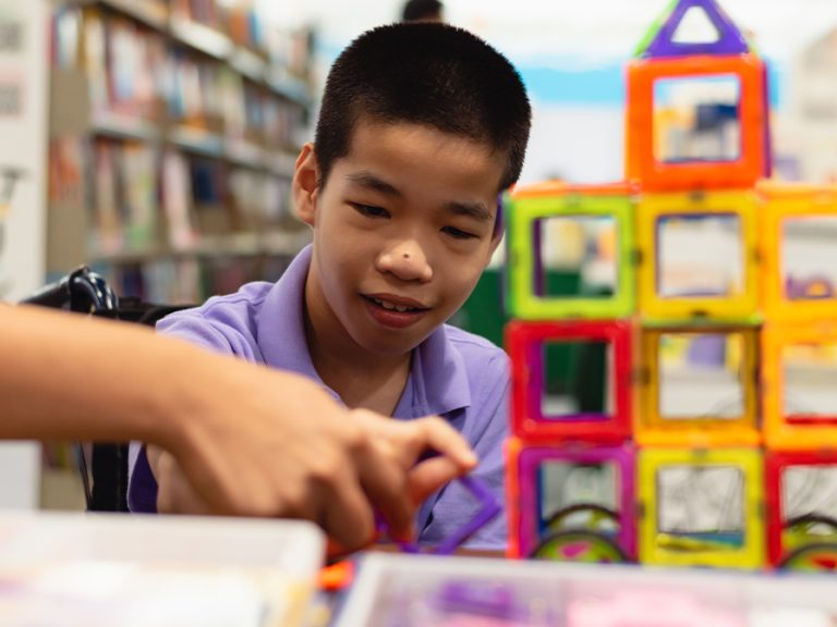 SEND child in a wheelchair being shown and enjoying playing with colourful building tiles and toys. Image: AnnGaysorn/Shutterstock