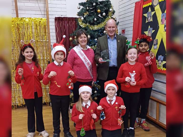 Pupils from Scott Primary School are pictured in front of a Christmas tree, being presented their Bedford Christmas Tree Festival Junior Trophy by Nick Kier of Lane & Holmes Estate Agents