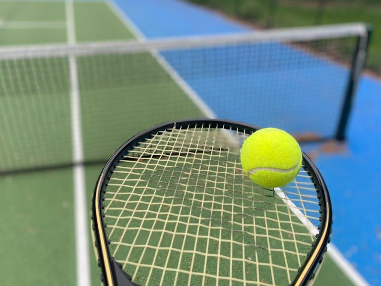 A tennis racquet and ball with a tennis court in the background.