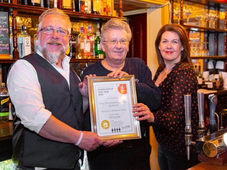 Ronnie. left and Rebecca, right, landlord and lady of The Devonshire Arms holding up their North Beds CAMRA Town Pub of the Year award