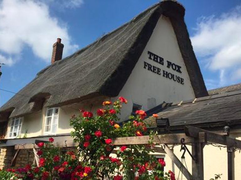 Exterior of the Fox at Carlton with its thatched roof and surounded by roses