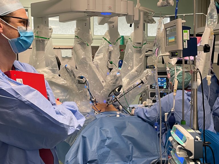 The da Vinci Xi robot being used at Bedford and L&D hospitals in action. It has arms covered in surgical protective plastic above a patient on a surgical bed. A surgeon is operating the robot. Image: Bedfordshire Hospitals NHS Foundation Trust