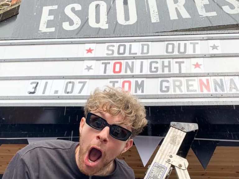 The singer/songwriter Tom Grennan at the top of a step ladder by the Esquires' sign where it says "SOLD OUT TONIGHT TOM GRENNAN"