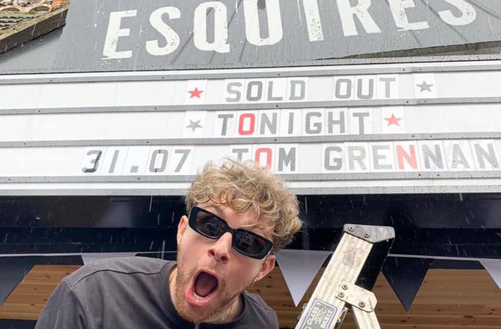The singer/songwriter Tom Grennan at the top of a step ladder by the Esquires' sign where it says "SOLD OUT TONIGHT TOM GRENNAN"