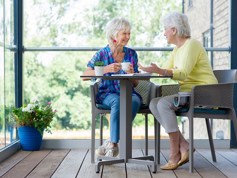 Two retired ladies enjoying a coffee and a chat on a balcony at a Hamberley Care Home. Image: Hamberley Care Homes
