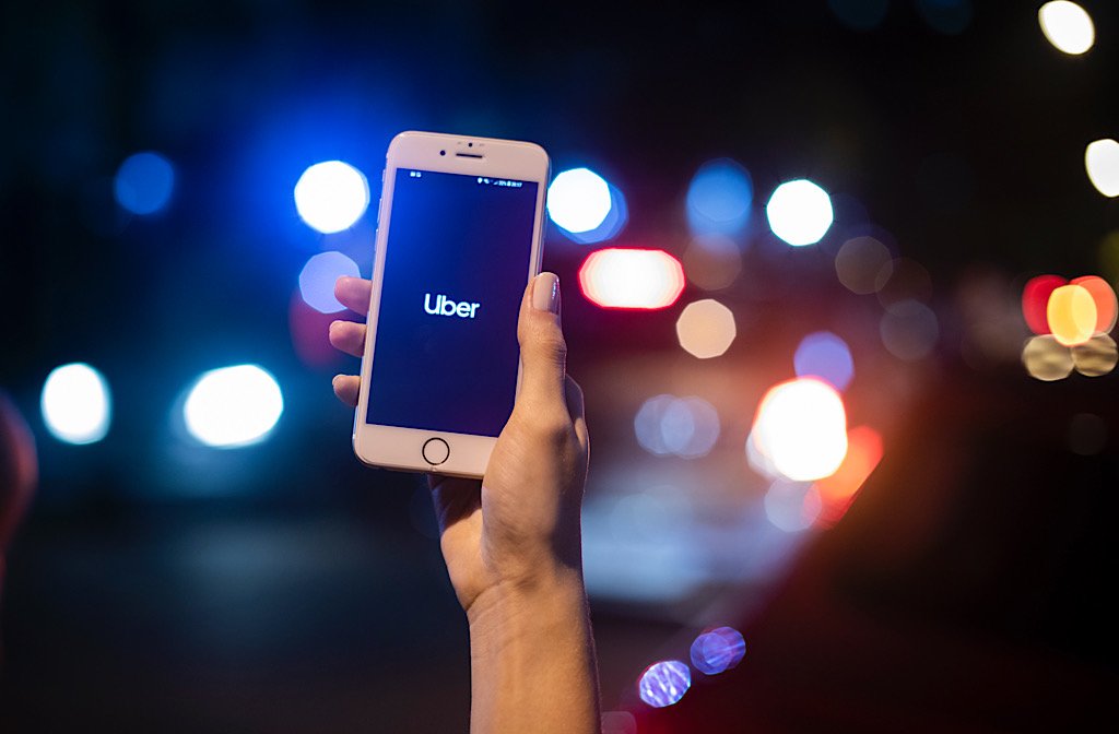 A mobile phone being held in hand. The phone is displaying the Uber logo