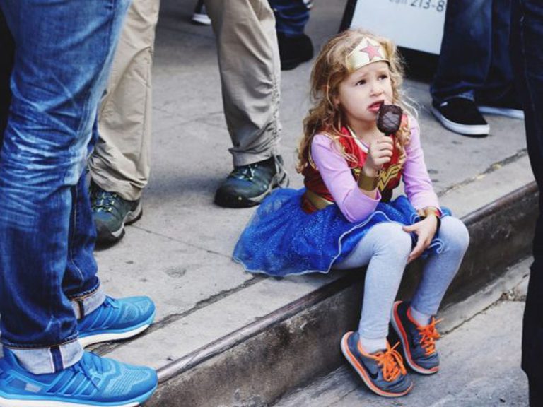 Young Achiever girl in superhero costume eating ice cream on some steps