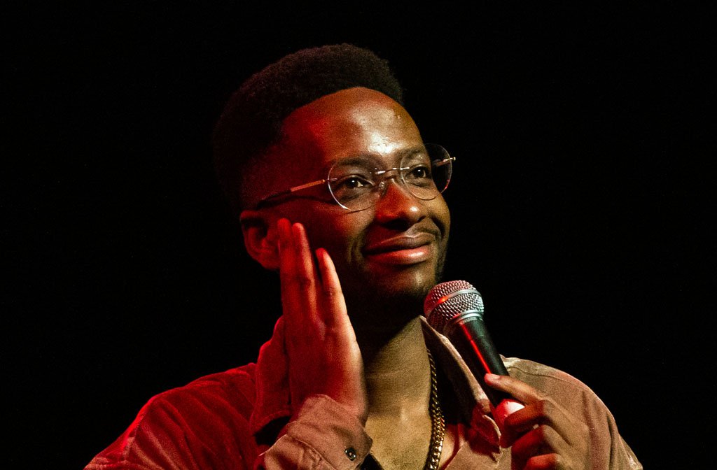 A close up photo of stand up comedian Tadiwa Mahlunge holding a microphone
