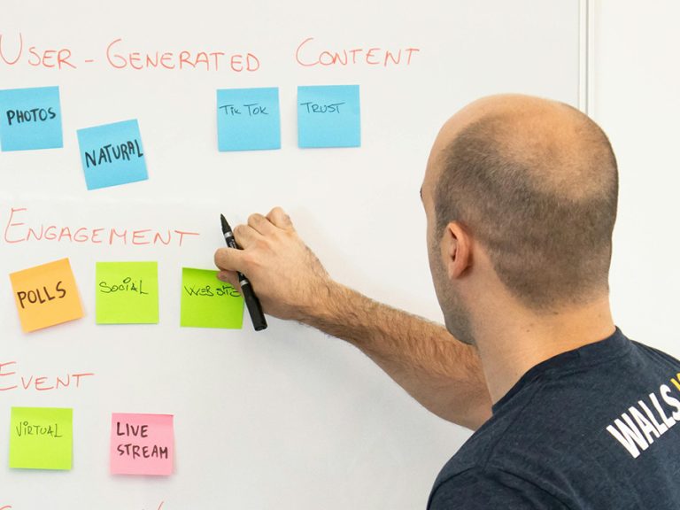 A Man with Sticky Notes by a Whiteboard looking at content options for marketing Image Walls.io Pexels