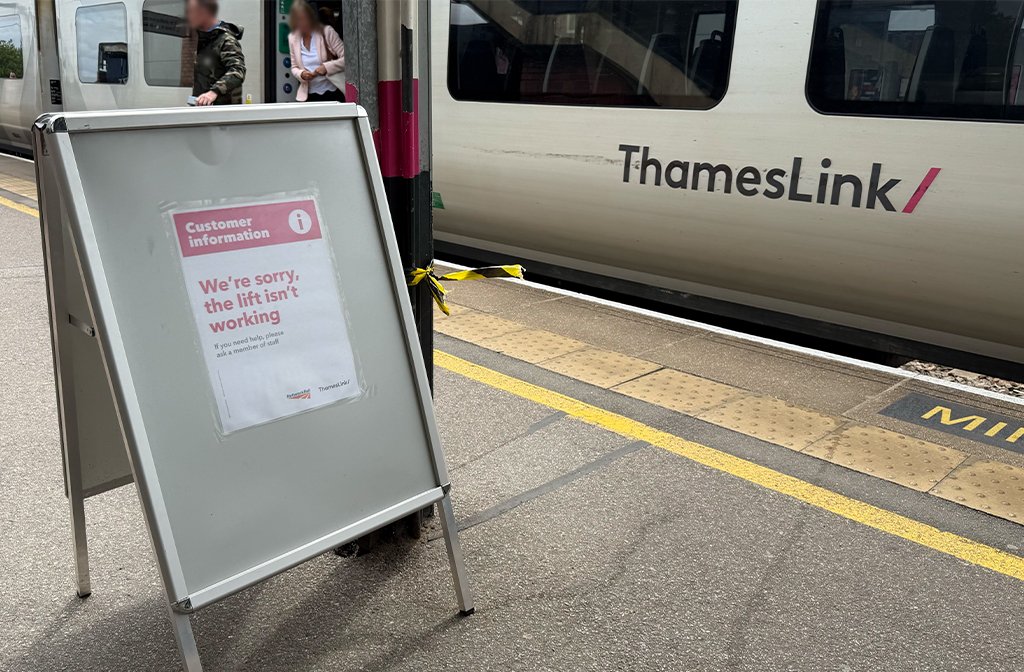 A sign warning train users that the lift at Bedford Train Station is out of order. Passengers are getting off a Thameslink train in the background.