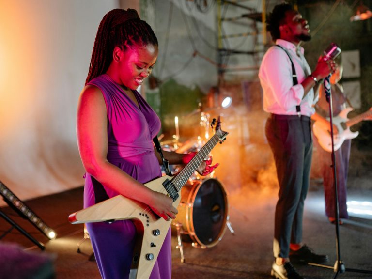 A man and woman perform live music on stage. She is playing a flying V guitar and he is singing into a microphone