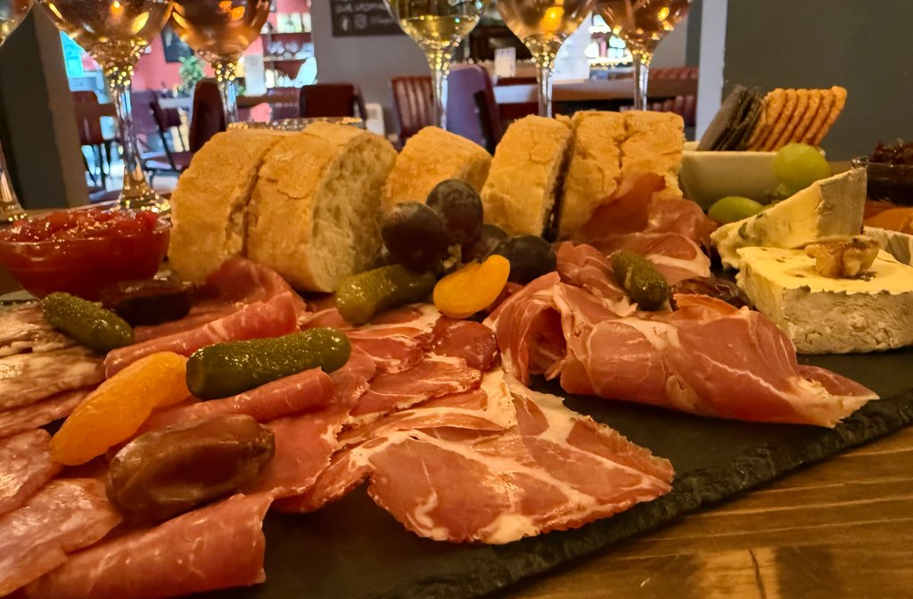 A close up of the charcuterie and cheese sharing platter from the Blue Glass featuring French bread, cheese, cold meat and gherkins