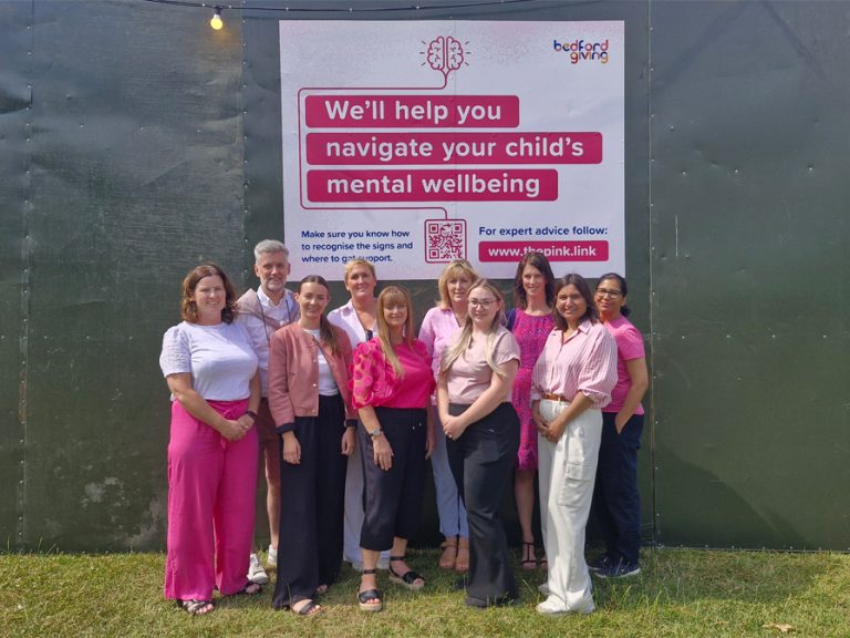 The Bedford Giving team at Bedford Summer Sessions in front of their Follow The Pink Link campaign posters
