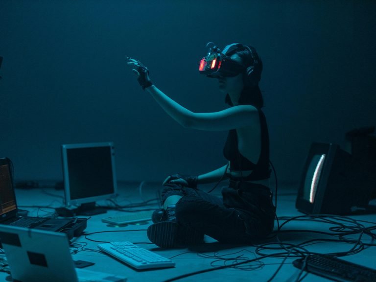 A Woman in a Tank Top Using a VR Headset surrounded by laptops, wires and keyboards Image cottonbro studio Pexels