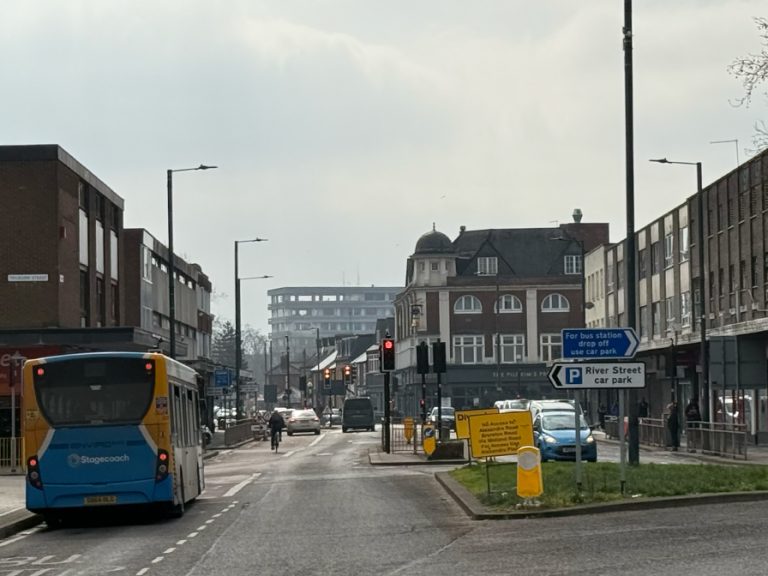 Greyfriars leading to River Street and Midland Road. A bus has stopped at the bus stop just before the traffic lights, there are multiple cars driving along the road and a cyclist is riding in the bus lane on the left. The Pilgrims Progress pub can be seen at the end of the road and Borough Hall can be seen in the distance. Image: Bedford Independent