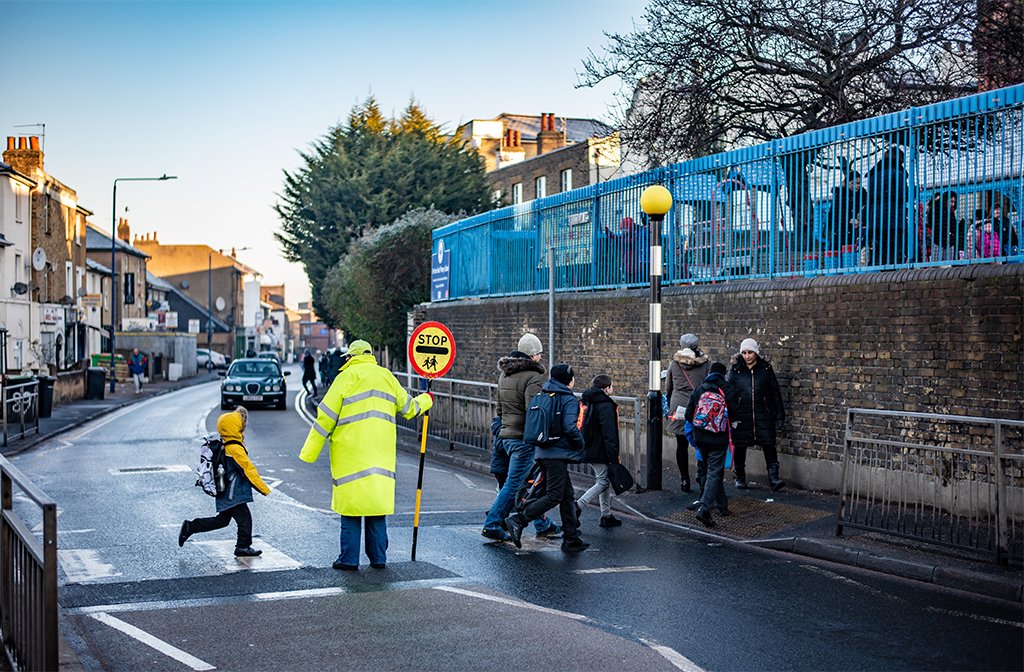 Lollipop person with the stop sign, helping children cross the street on the pedestrian crossing. Image Mariusz Zawadzki Shutterstock