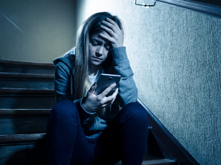 Teenage girl cyberbullying grooming abuse sitting on stairs alone and upset. Image: SB Arts Media/Shutterstock