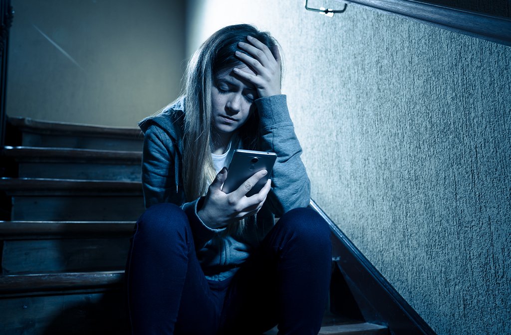 Teenage girl cyberbullying grooming abuse sitting on stairs alone and upset. Image: SB Arts Media/Shutterstock