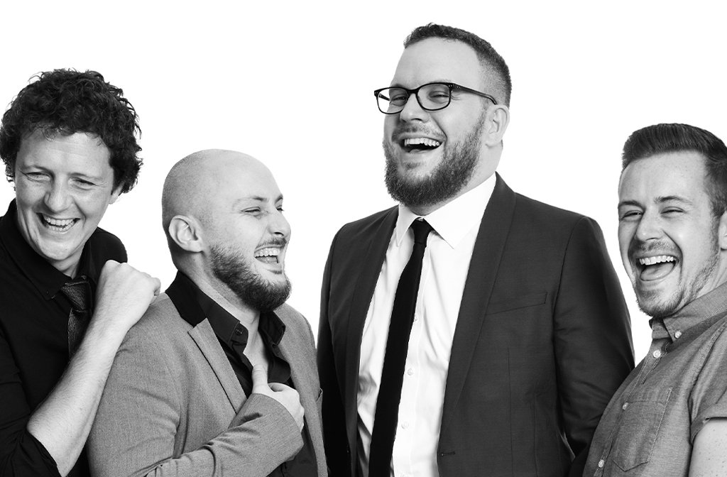 A black and white photo of the four members of improv comedy group The Noise Next Door. They are all laughing