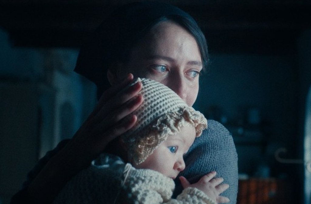 A woman cradles the head of a baby in a bonnet as they appear to be hiding from someone or something