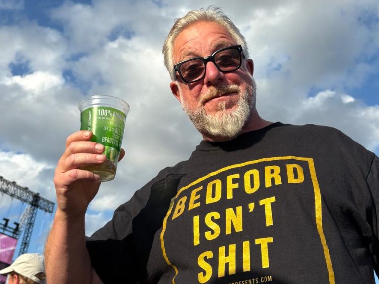 A photograph of Ronnie Toms, landlord of the Devonshire Arms holding a glass of beer and wearing a t-shirt that says Bedford Isn't Shit