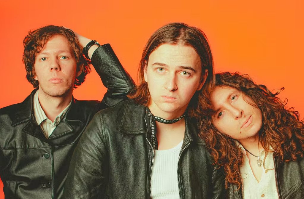 The three members of The Howlers are photographed against a bright orange background