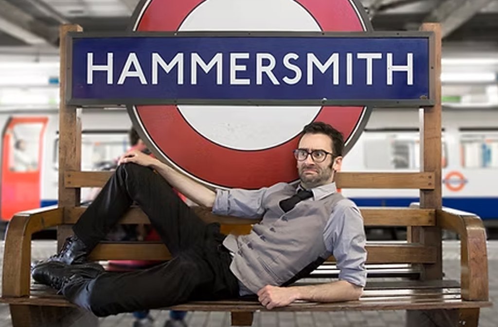 The comedian MC Hammersmith, reclining on a bench on the platform of Hammersmith tube station