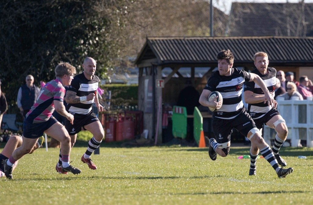 A Bedford Ath rugby player runs clear of an Olney defender in March 2026