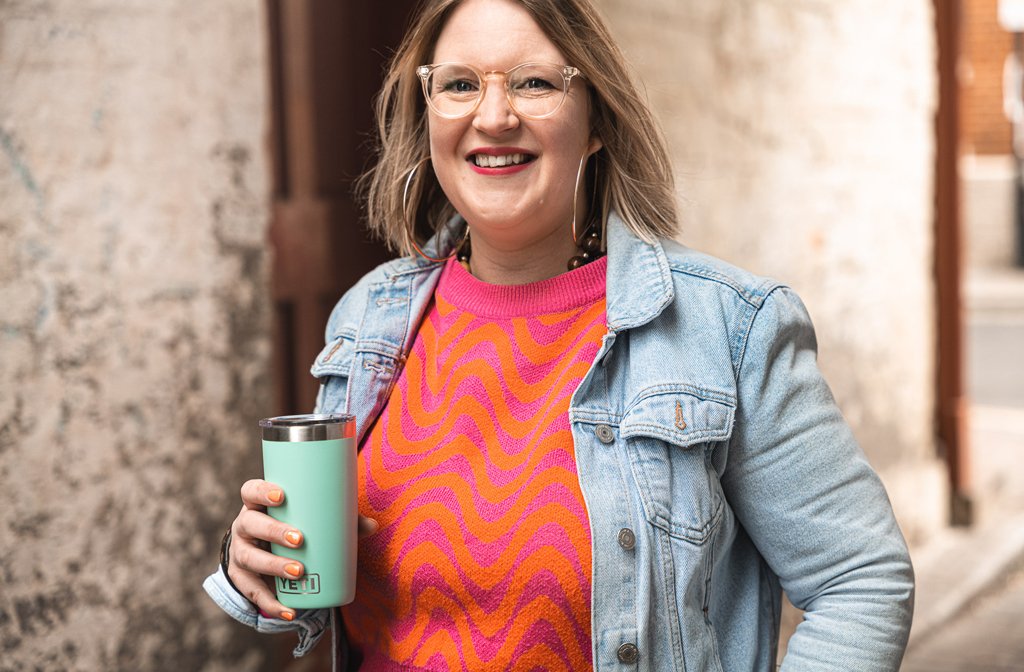 Carly Cook, photographed in an orange and pink sweater and denim jacket