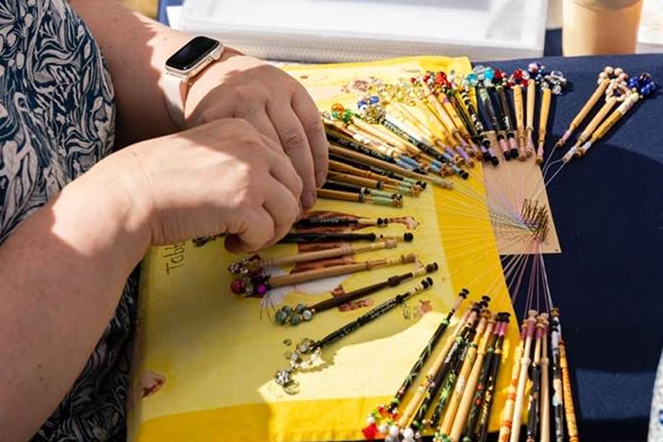 The hands of a woman making traditional lace using bobbins on a cushion