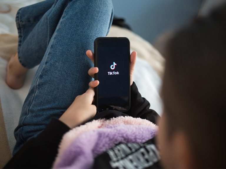 Child with phone in his hands lying at home on bed. Social Media tiktok is loaded on screen