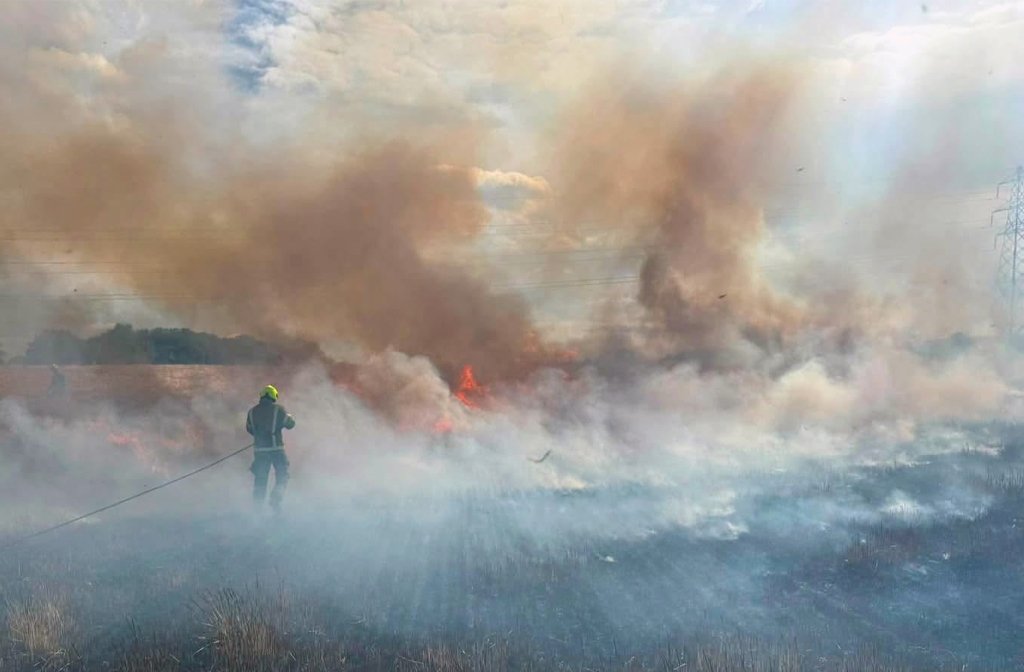A Bedfordshire firefighter surrounded by smoke tackles a wildfire in an open field Image BFRS