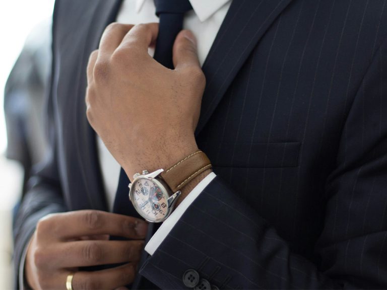 A man wearing an expensive watch and in a designer suit adjusting his tie Image Ruthson Zimmerman Unsplash