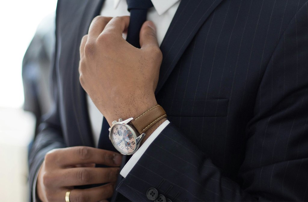 A man wearing an expensive watch and in a designer suit adjusting his tie Image Ruthson Zimmerman Unsplash