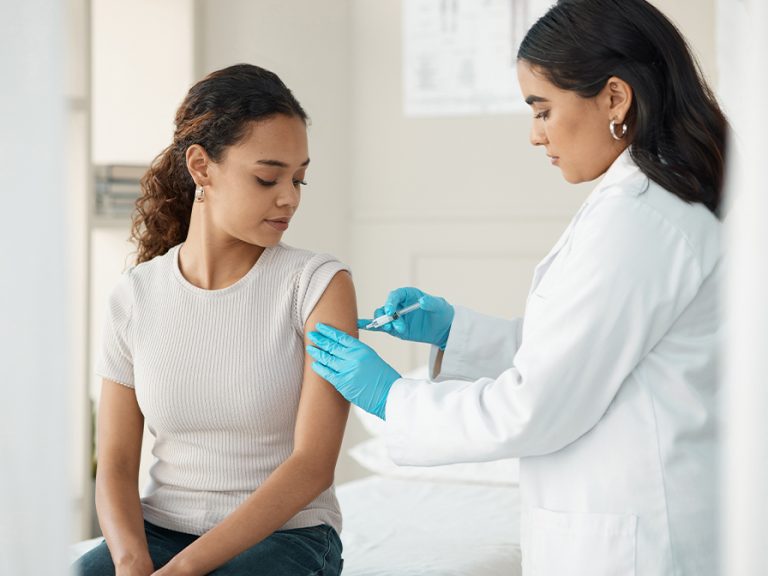 A young woman receiving a vaccine injection from a healthcare worker. Image: PeopleImages/Shutterstock