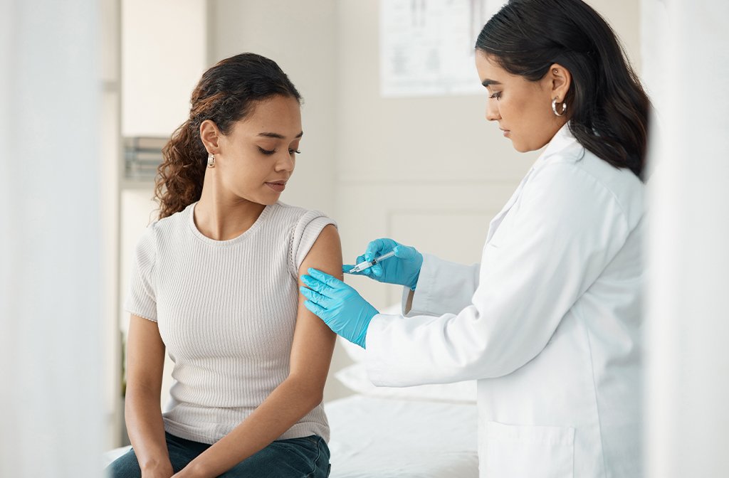 A young woman receiving a vaccine injection from a healthcare worker. Image: PeopleImages/Shutterstock