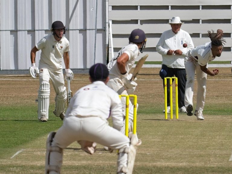 A Bedfordshire bowler bowling at a Norfolk batter at Sprowston Cricket Club in Norfolk, with the wicket keeper waiting in the foreground