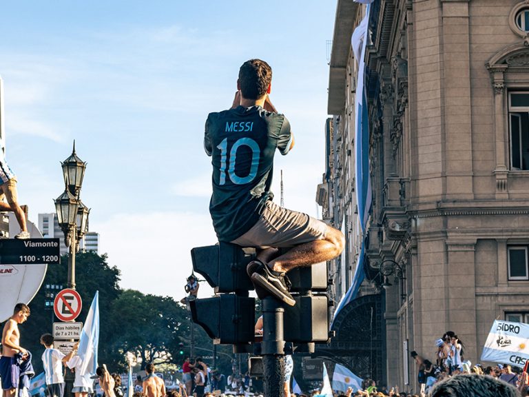Crowd celebrating in Buenos Aires after Argentina's 2022 World Cup win with a fan in a Messi shirt climbing a lamp post Image: Fabrizio Velez/Pexels